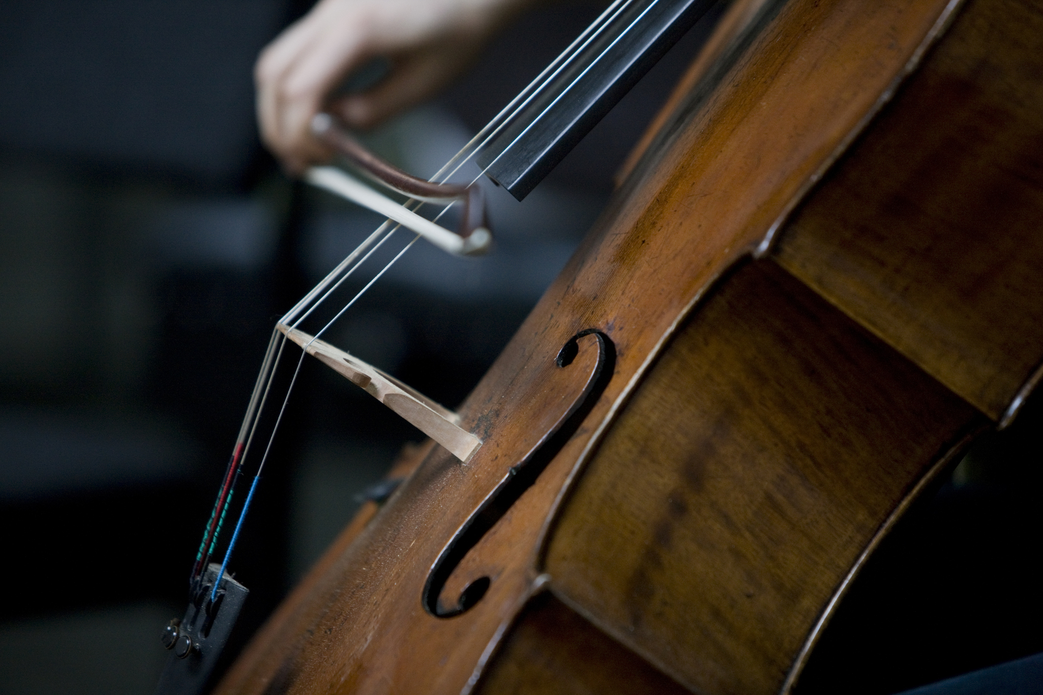 Close-up of a person&#x27;s hand playing the cello with a bow, focusing on strings and f-holes