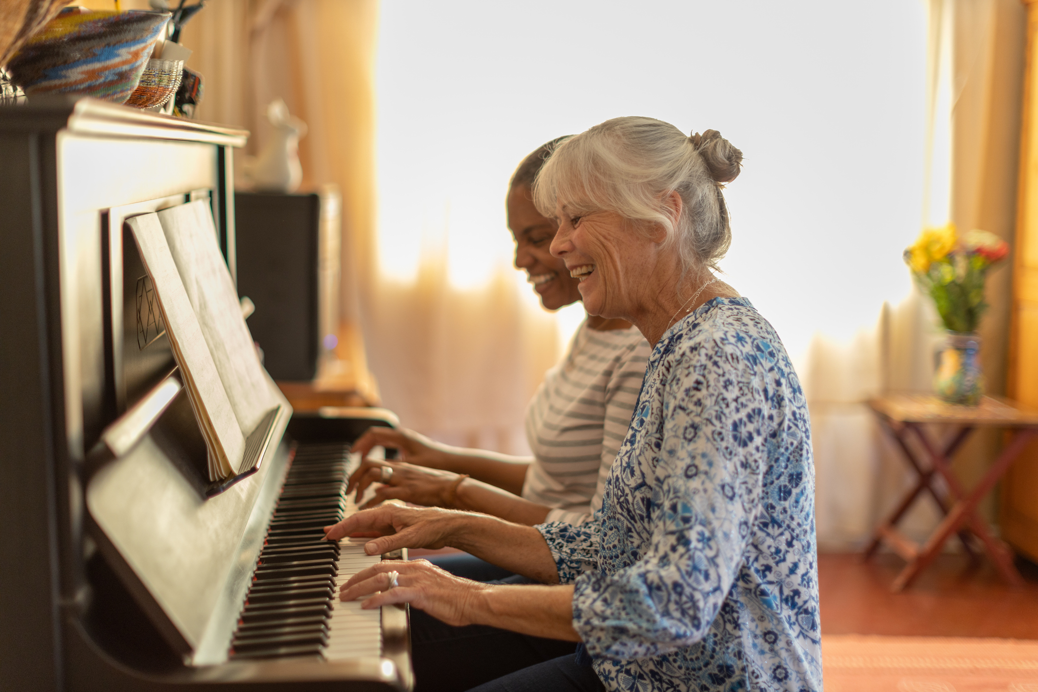 Two older women sitting and playing piano while smiling