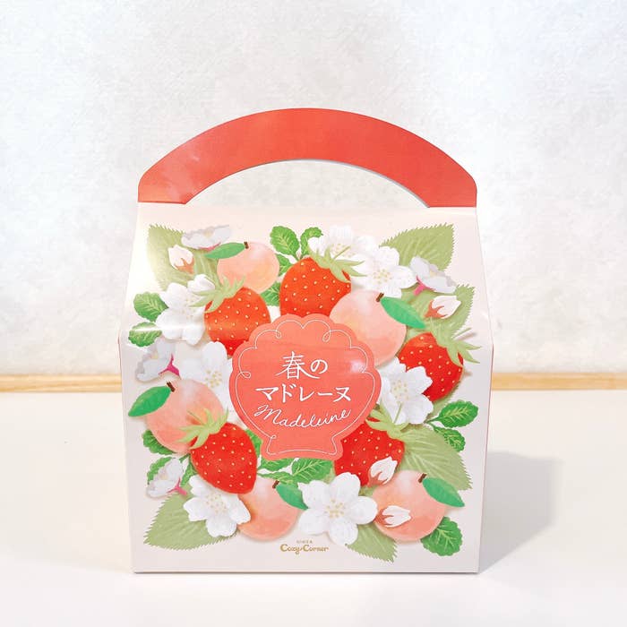 A paper gift bag with floral and strawberry design and Japanese text, alongside "Madeleine" written in English