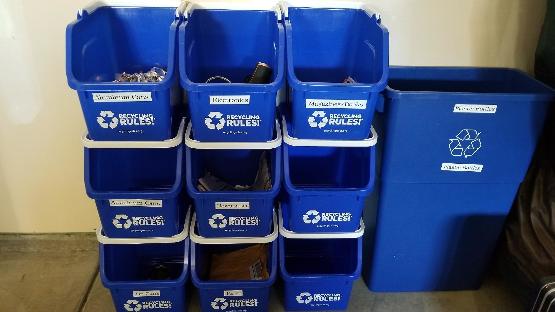 Recycling bins labeled for aluminum cans, electronics, and paper alongside a large plastic recycling bin