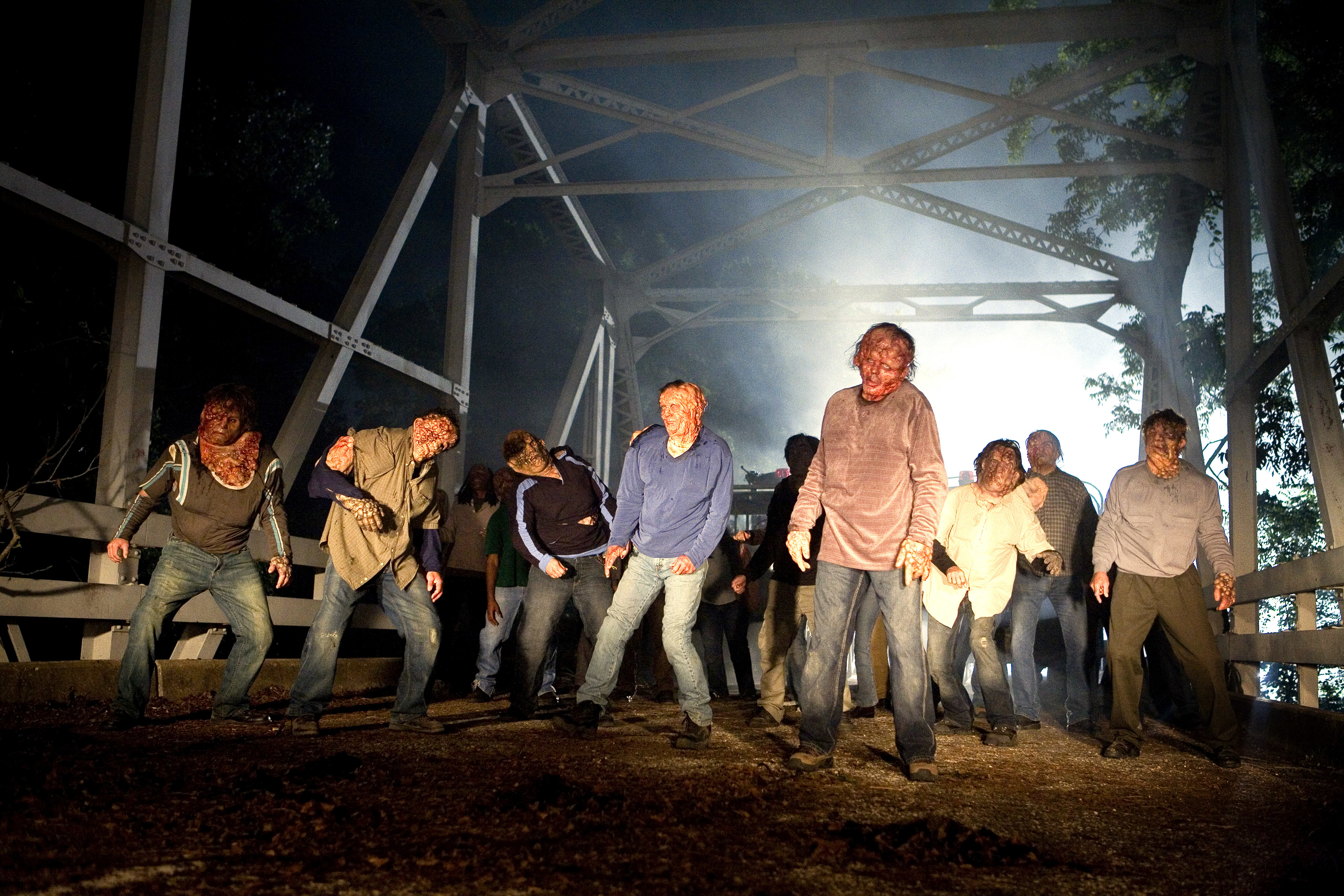 Group of people walking under a bridge, disheveled, as if in a scene from a thriller or horror TV show or movie