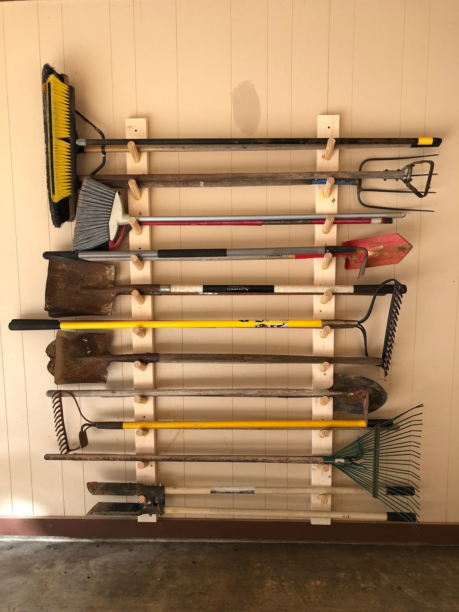 Assorted garden tools including shovels and rakes hung neatly on a garage wall