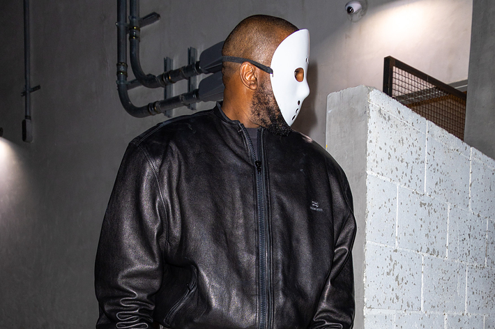 Musician in a leather jacket and mask standing by a wall