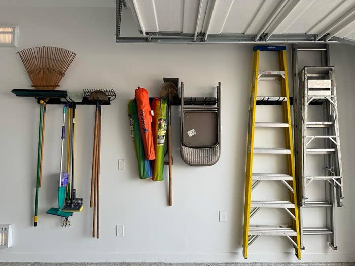 Wall-mounted storage system holding a variety of garden tools and ladders