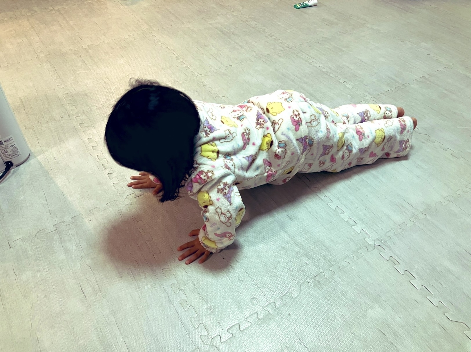 赤ちゃんがパジャマを着て床にうつ伏せになっている。