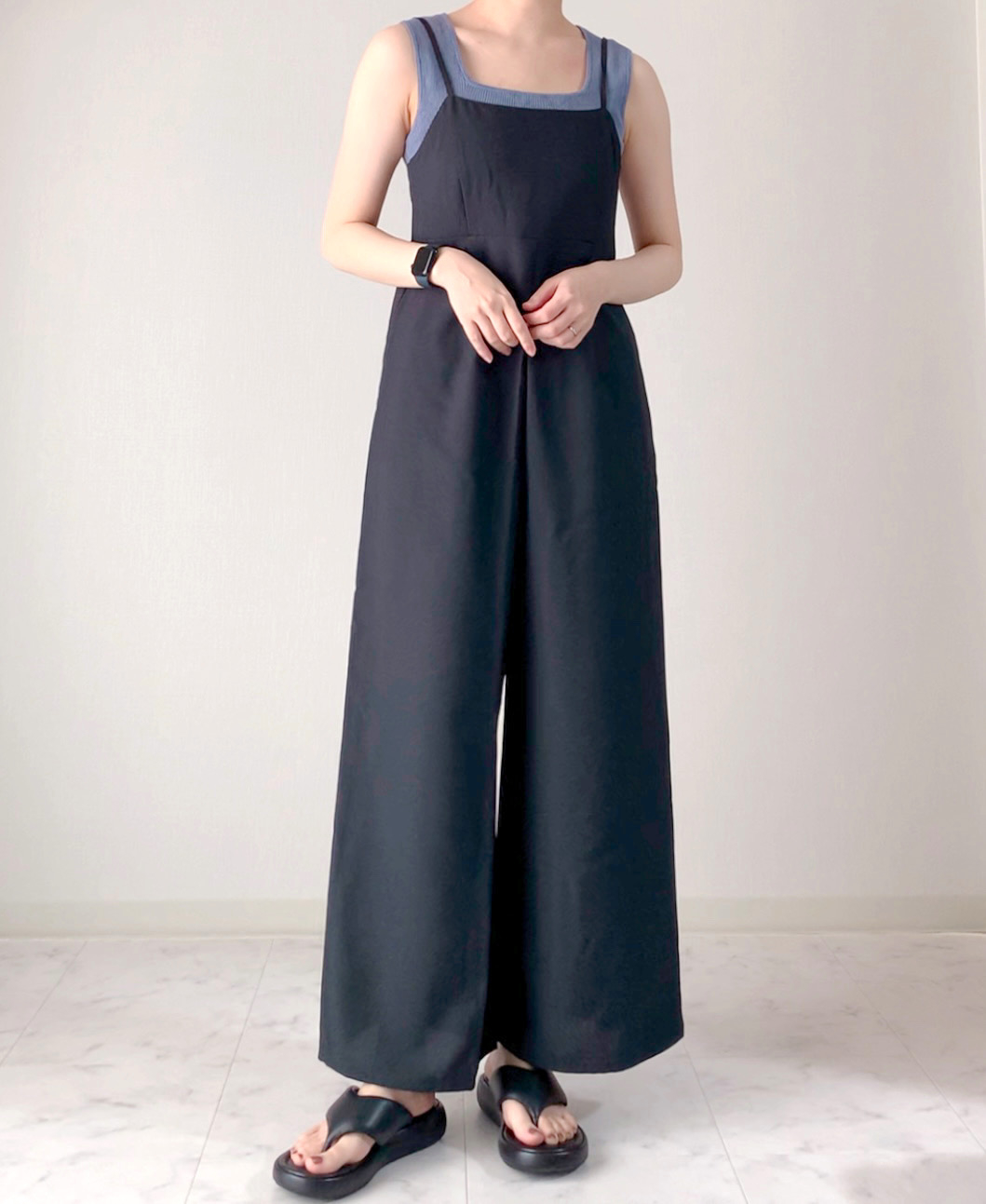 Person in a sleeveless jumpsuit with wide-legged pants, standing indoors, face not shown