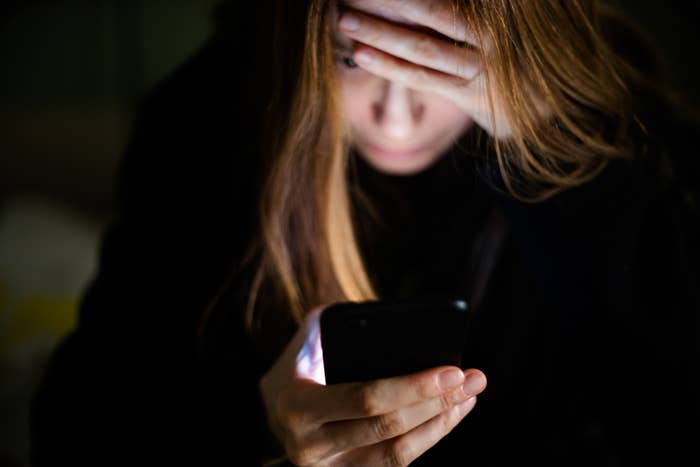 Person with hand on forehead looking at smartphone screen in a dimly lit environment