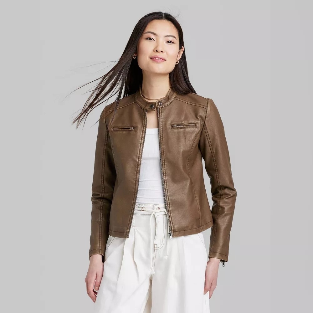 a model in a brown leather jacket and white top, and white pants