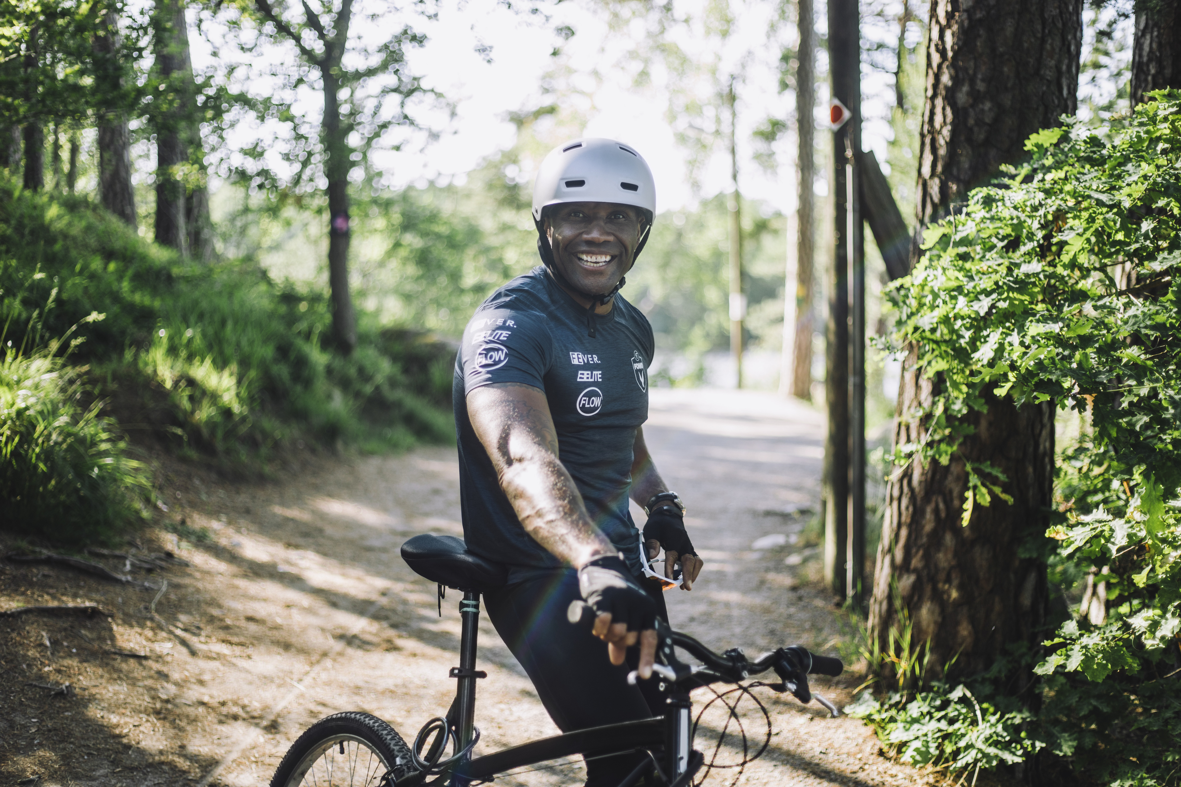 Person with helmet sitting on a bike, smiling, on a forest path