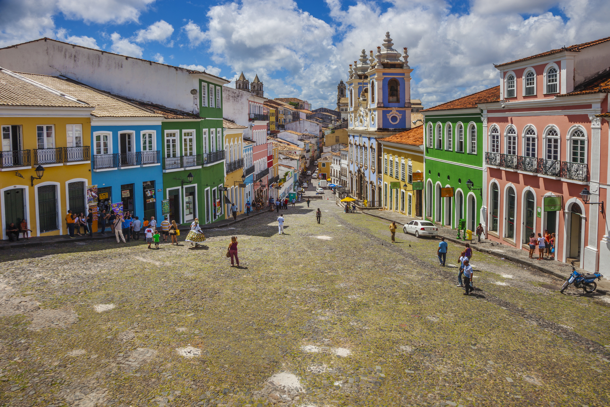 Pedestrians and cyclists on a broad cobblestone street flanked by colorful colonial buildings
