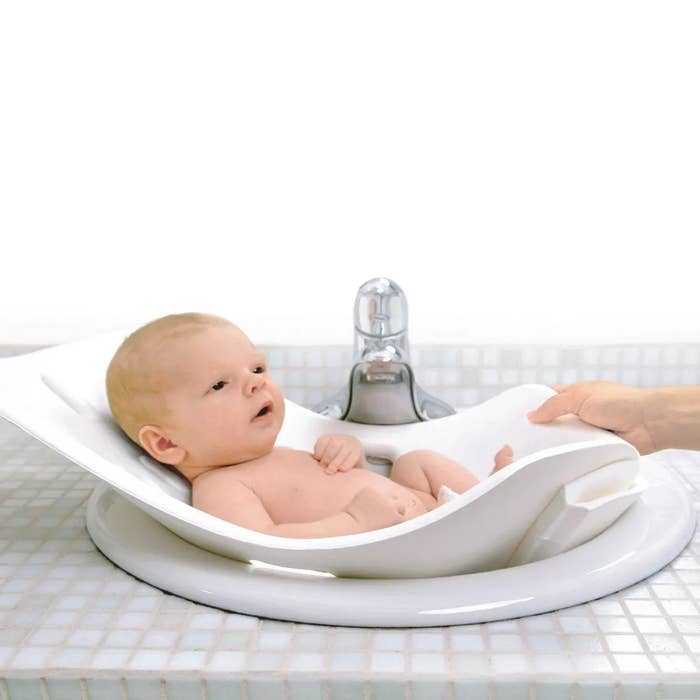 Infant in a bath support in a sink with an adult&#x27;s hand gently touching the side