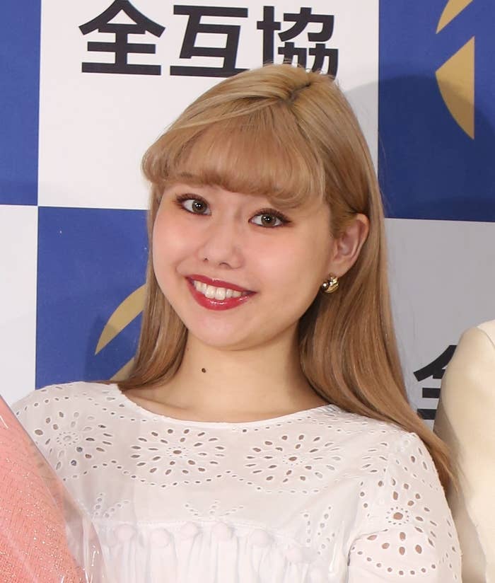 写真には笑顔の女性が白い衣服を着てカメラを見ています。