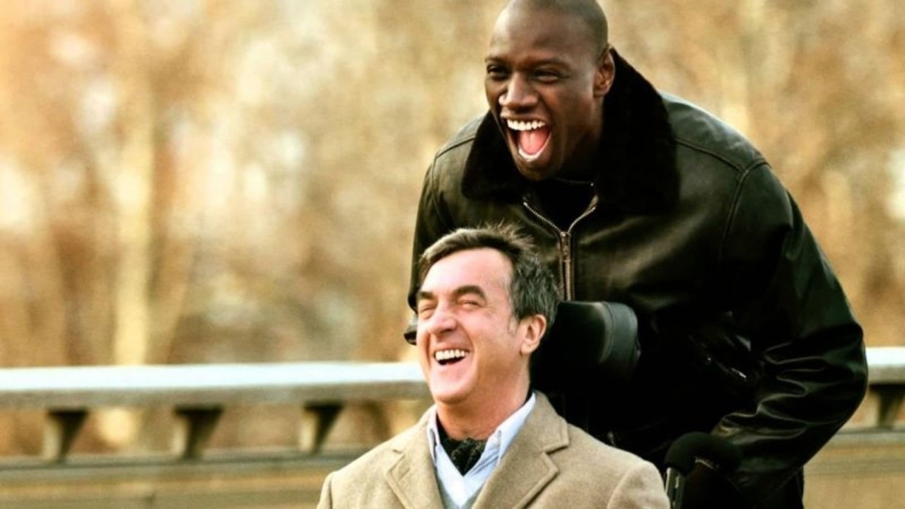 Two men, one seated in a wheelchair, the other standing behind, both laughing joyfully