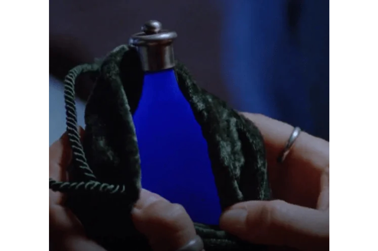 Close-up of a person&#x27;s hands holding an ornate green flask with a blue liquid visible