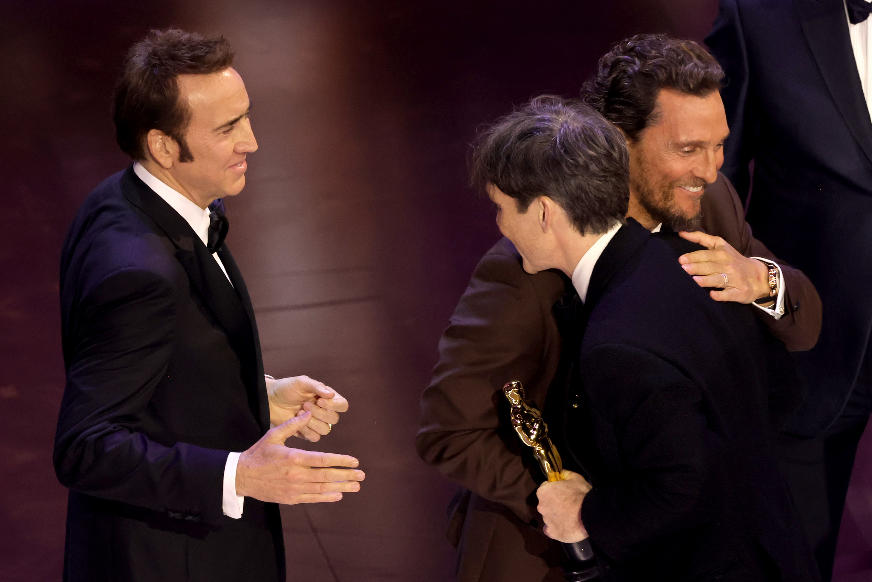 Cillian Murphy hugging Matthew McConaughey as he accepts his Oscar as Nicholas Cage looks on