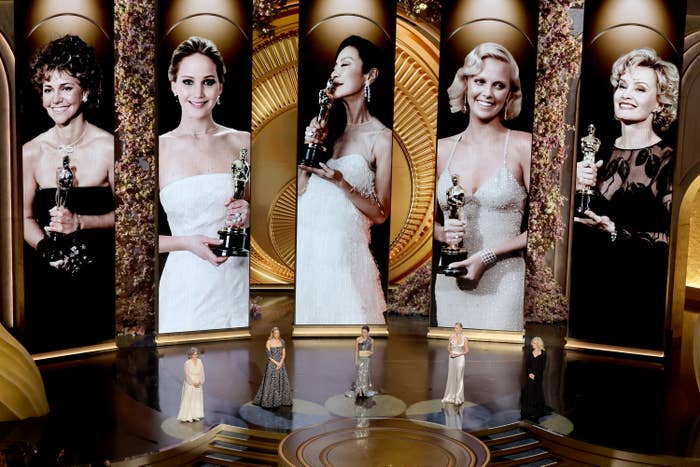 Five actresses with Oscars on stage, each spotlighted by historical winner portraits in the background