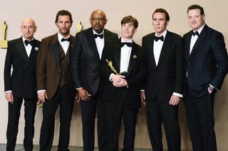 Five men in formal suits, one holding a trophy, posing together at an event