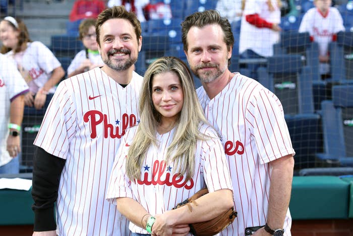 Rider Strong, Danielle Fishel and Will Friedle in Philadelphia Phillies baseball jerseys posing together on the field at a game