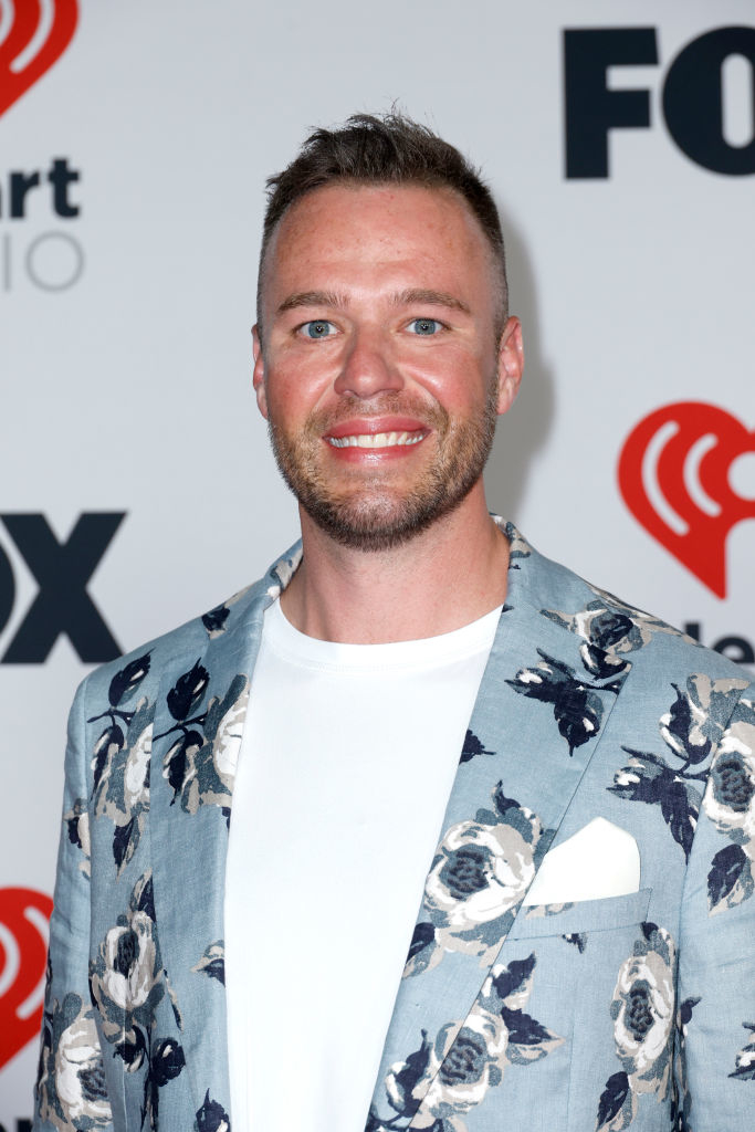 Nick in floral blazer at event with Fox and iHeartRadio logos in background