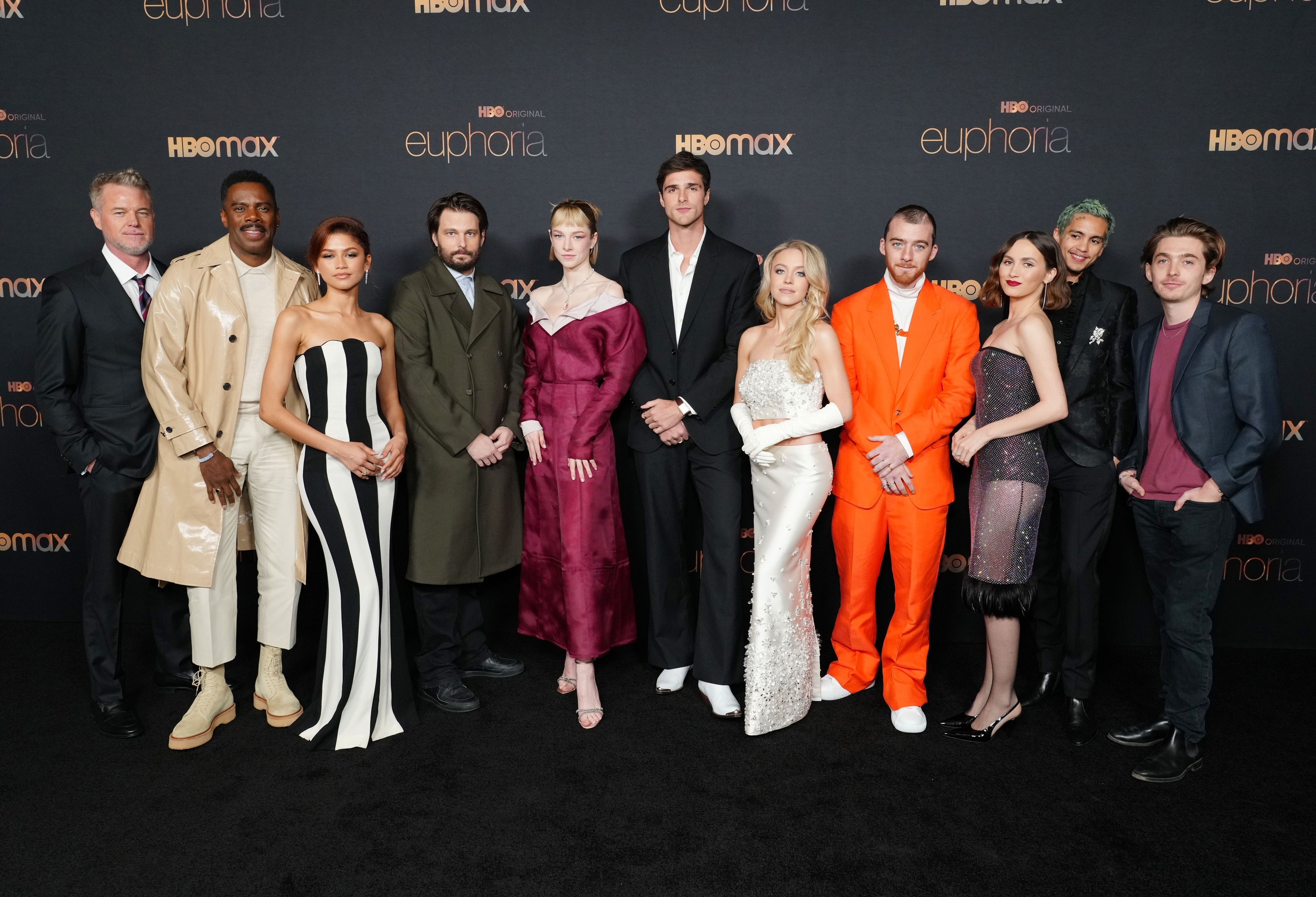 Group of cast members from &quot;Euphoria,&quot; standing together in formal attire on a black carpet before a promotional backdrop