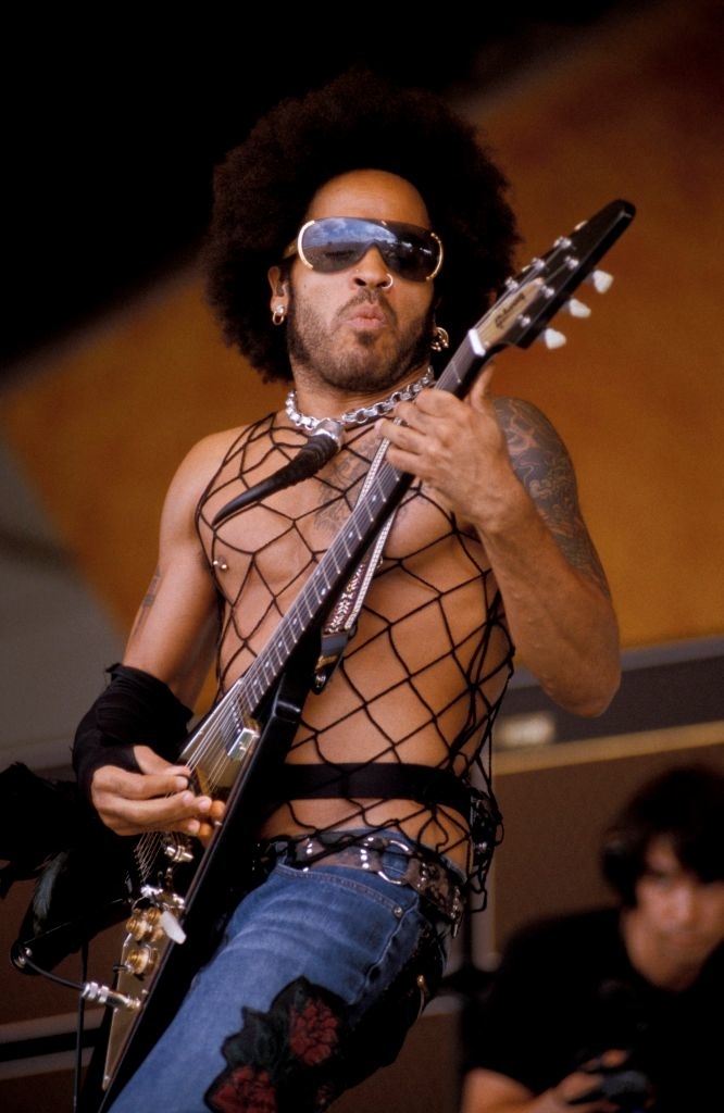 lenny in a mesh top and sunglasses playing electric guitar on stage