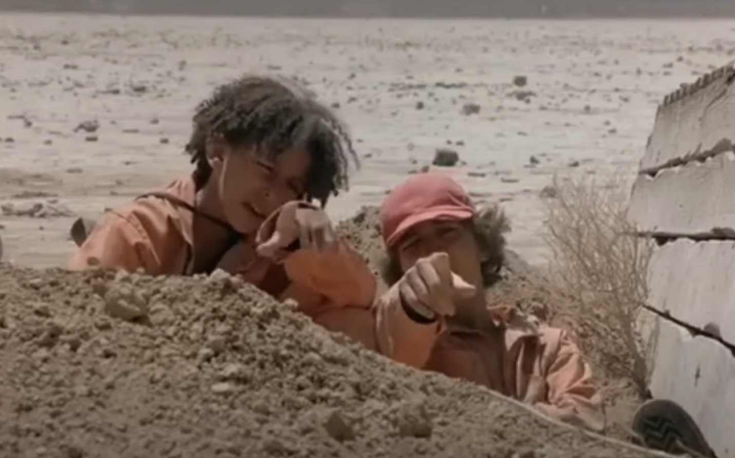 Two characters from the film &quot;Holes&quot; lie on the ground, pointing towards something outside of frame