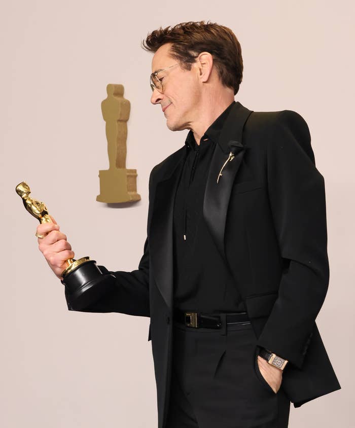 Robert Downey Jr. in a black suit holding an Oscar statue with another statue in the background