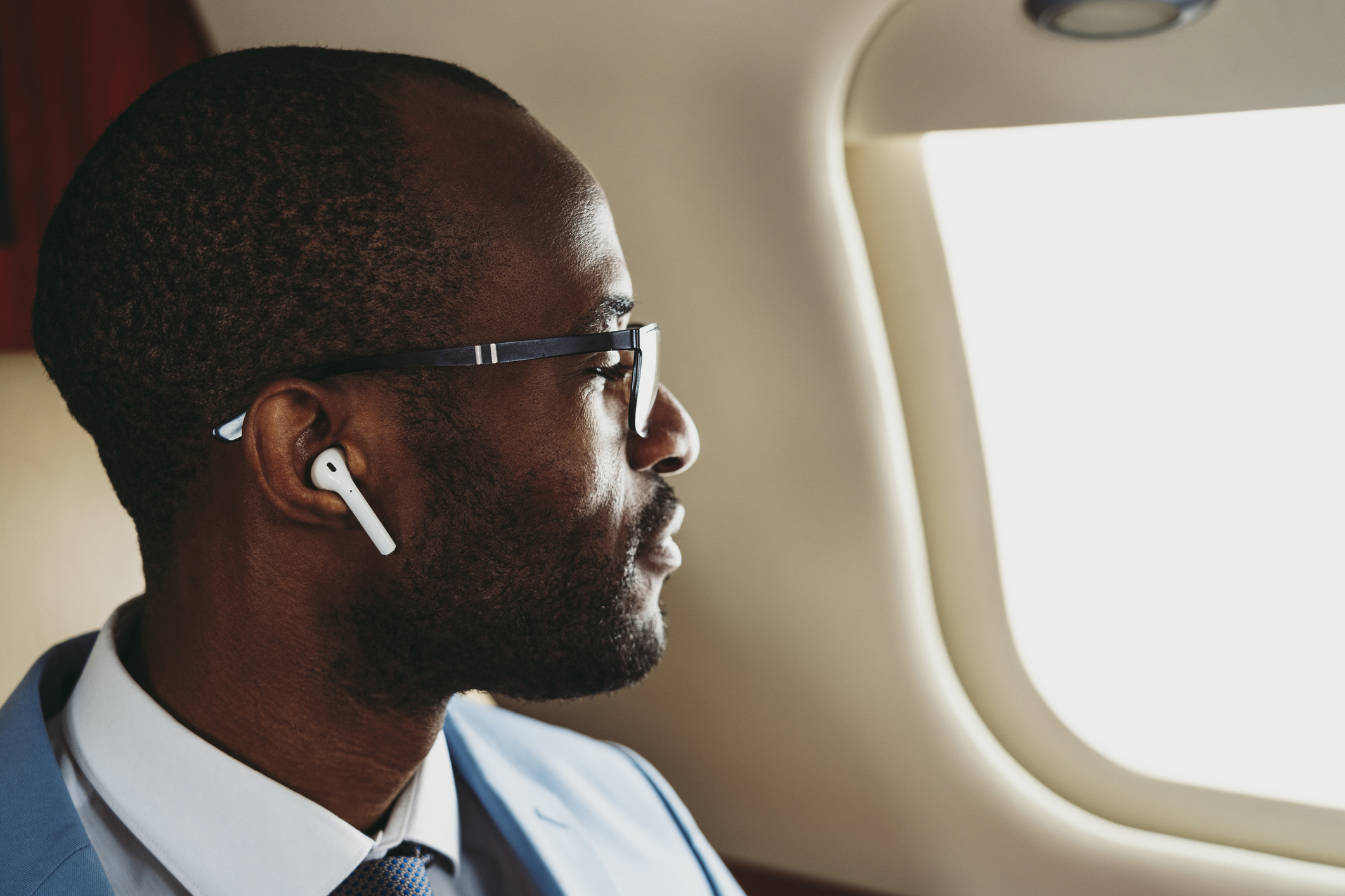 Man in suit with earphones looks out airplane window