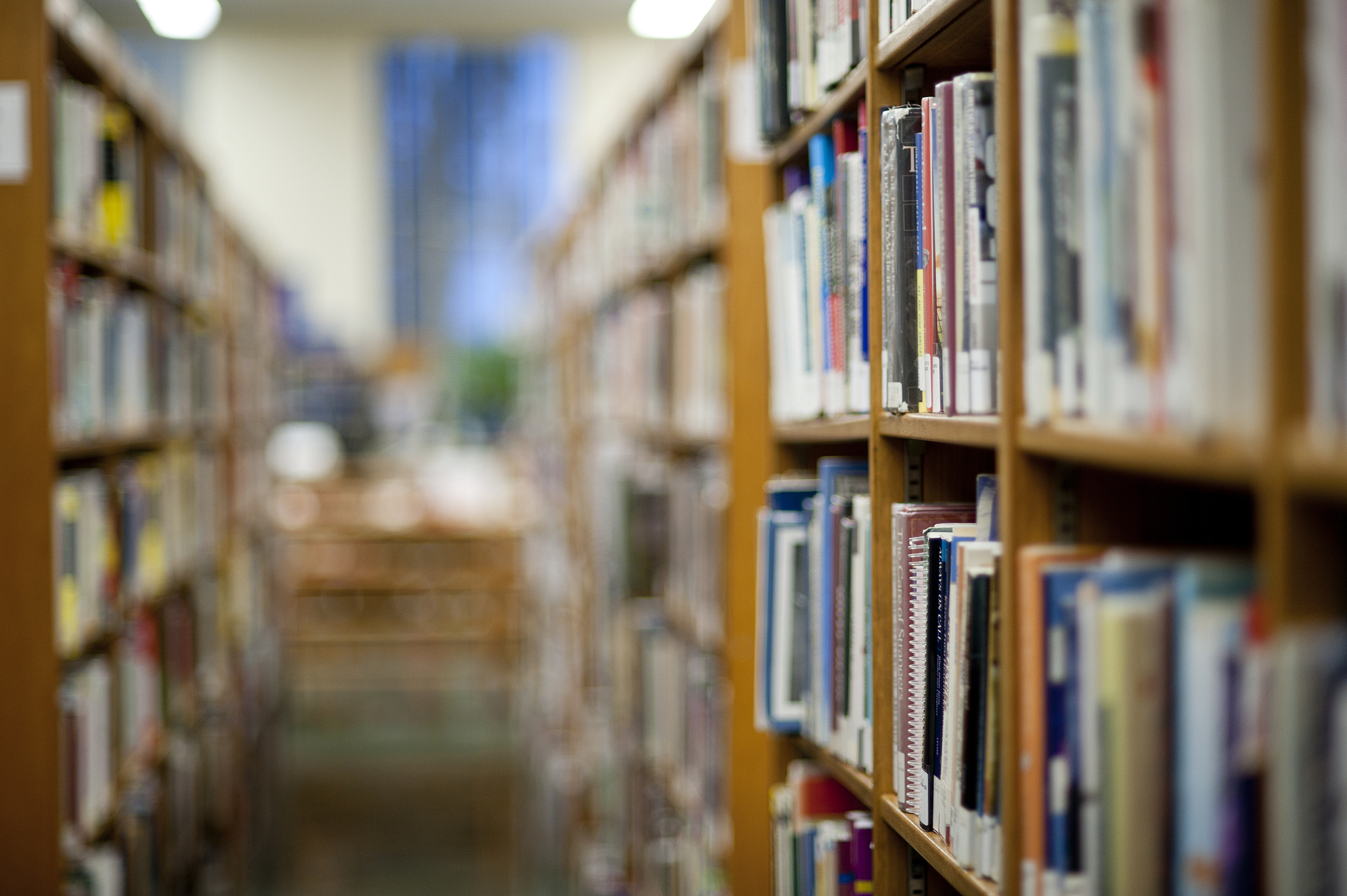 Aisles of bookshelves in a library, focus on books in the foreground with blurred background