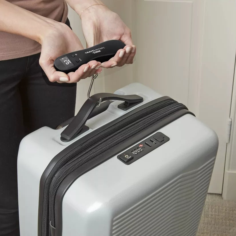Person using a digital luggage scale to weigh a suitcase before traveling