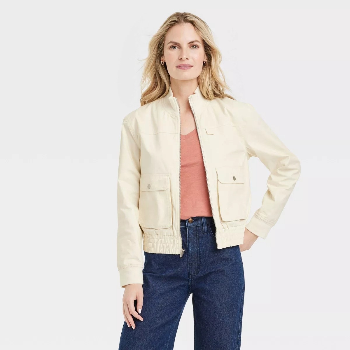 model in a casual cream jacket and jeans with hands in pockets