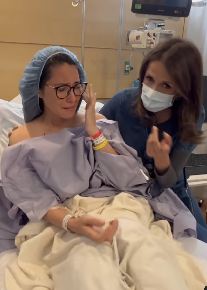 An emotional Olivia Munn in a hospital bed in a gown