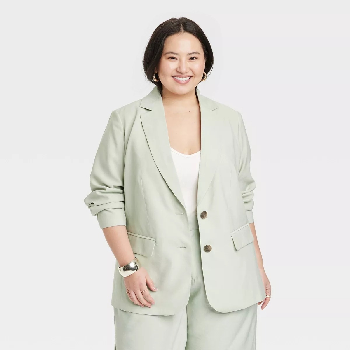 model in a casual light blazer and trousers with a white top, posing with hands in pockets