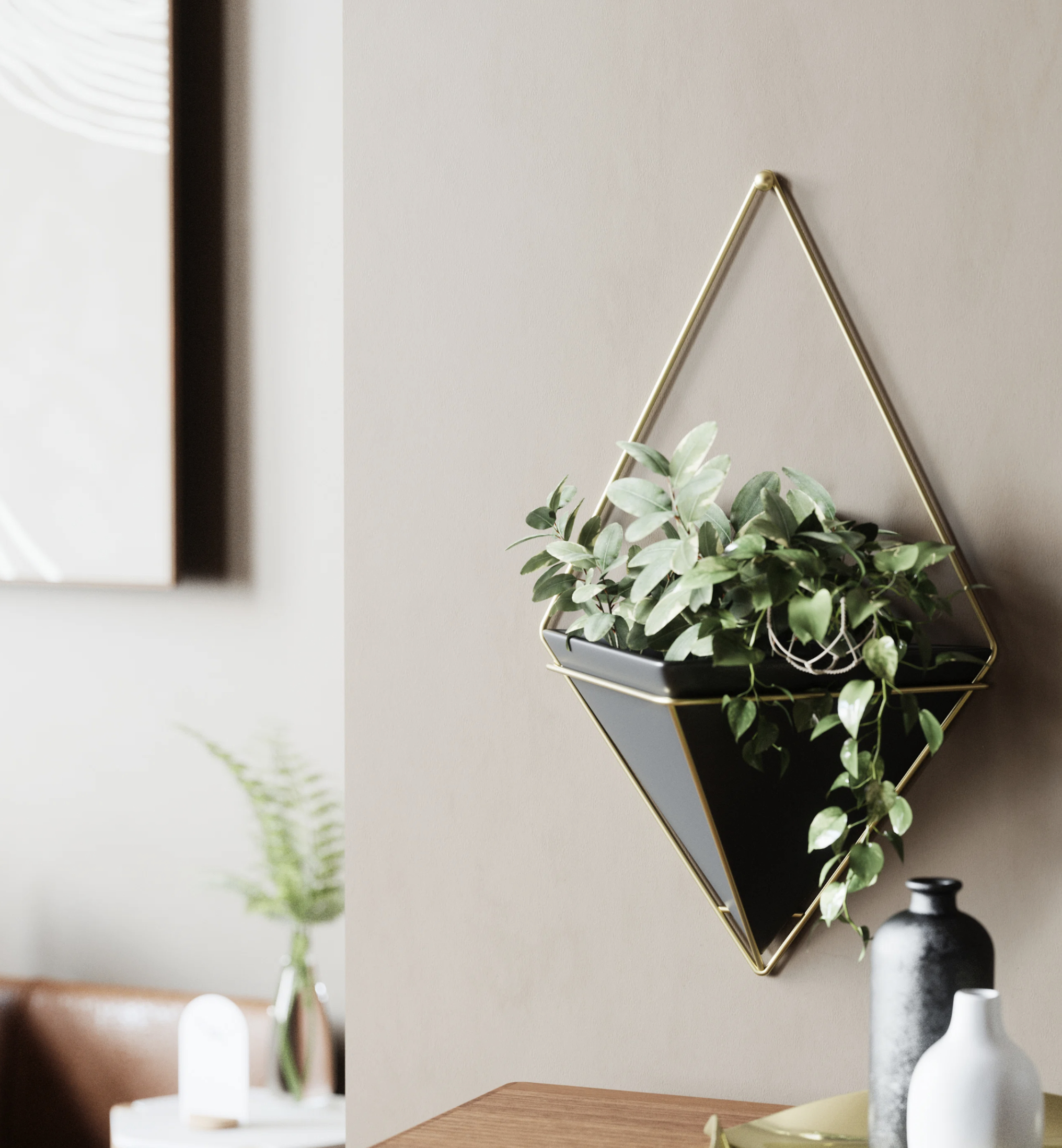 Geometric wall-mounted planter with cascading foliage, hung beside artwork