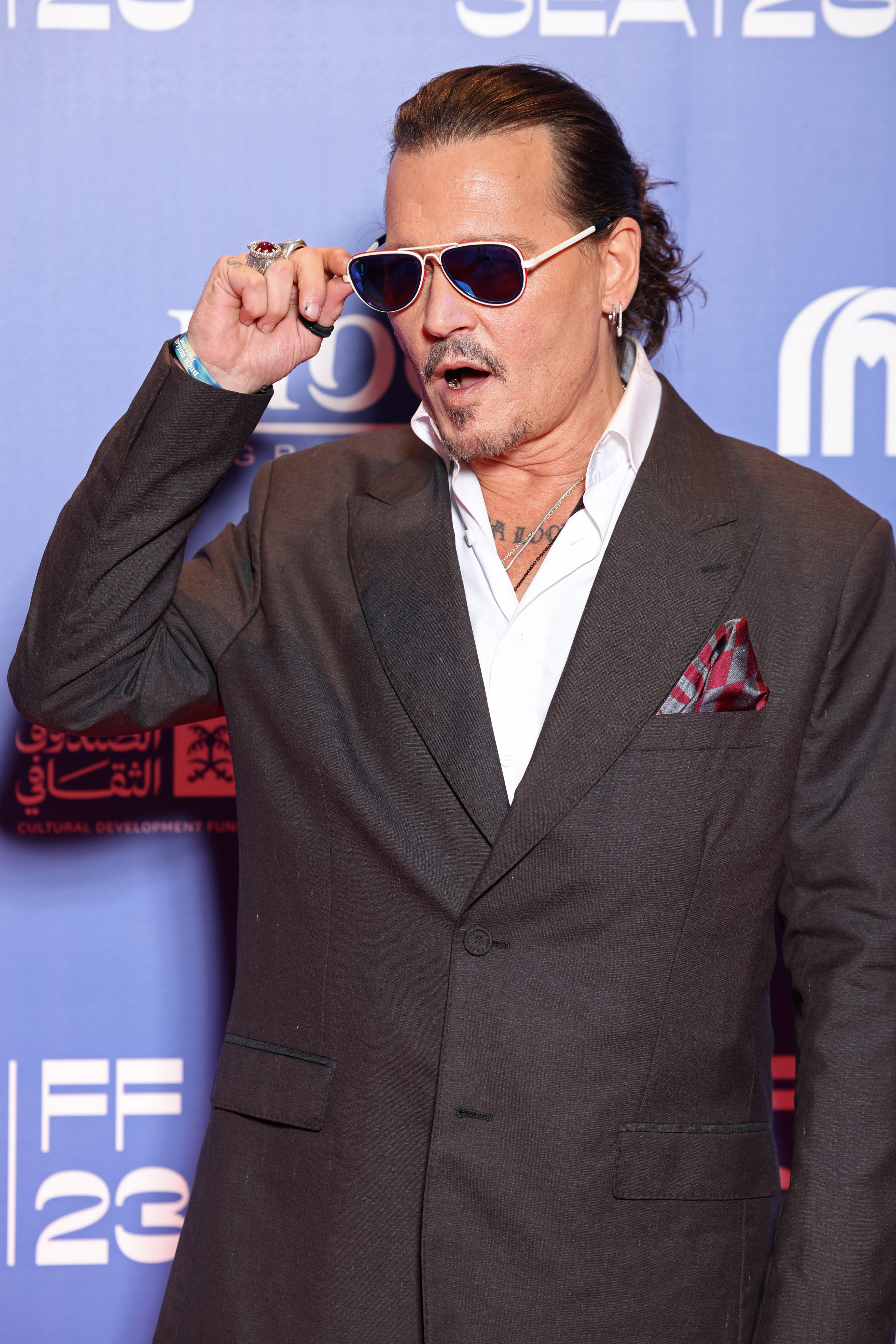 Johnny Depp in a grey suit, adjusting sunglasses, at an event