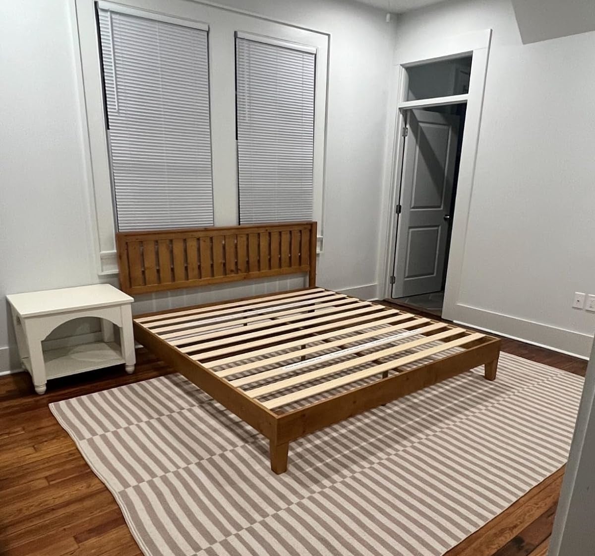 A minimalist bedroom with an unassembled wooden bed frame, a small bench, and a striped rug