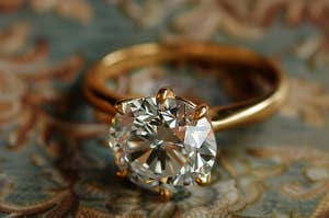 Close-up of a gold engagement ring with a prominent diamond, set against a floral patterned background