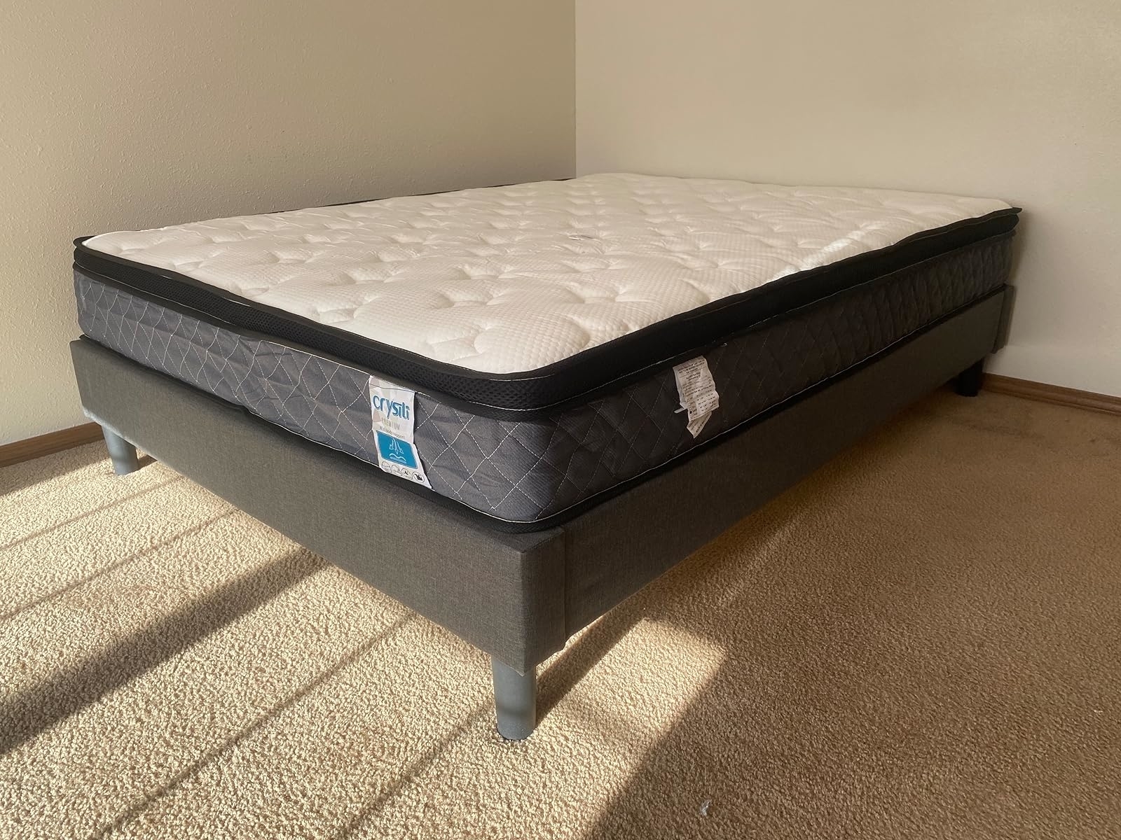 New mattress on a bed frame with tags attached, shown in a sunny room