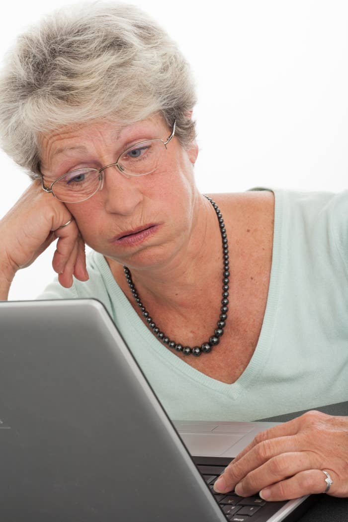 An older woman with glasses looking at a laptop screen with an exhausted expression