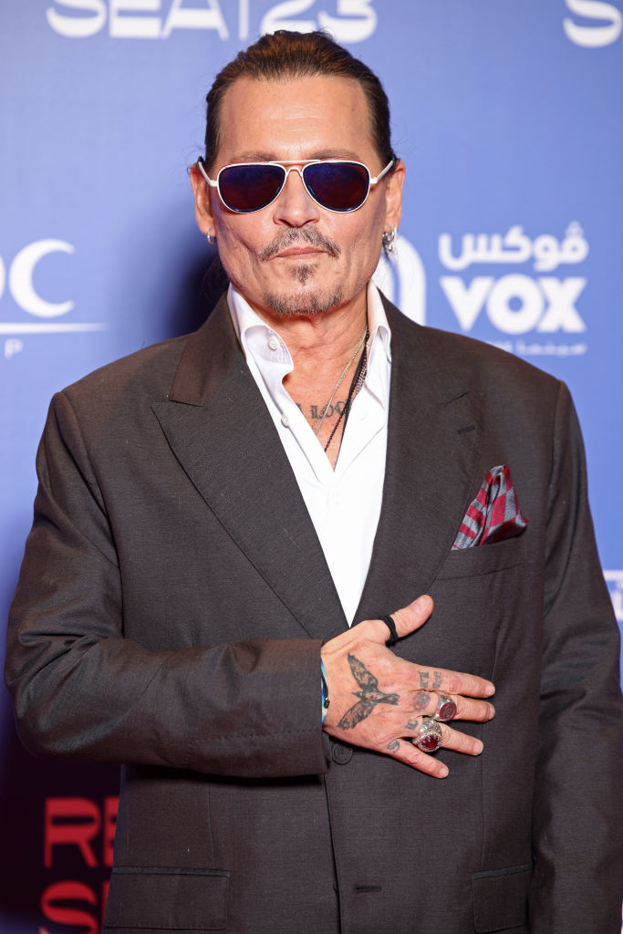 Johnny Depp poses in a suit with sunglasses; hand over heart gesture, at an event