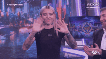 Mujer sonriendo y saludando con las manos en un programa de televisión