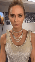 Emily in a glittery sleeveless dress moving from side to side to show off her raised shoulders, looking into the camera