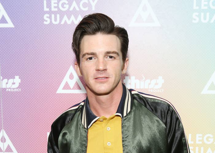 Drake Bell in a varsity jacket and polo shirt posing for photographers at a red carpet event