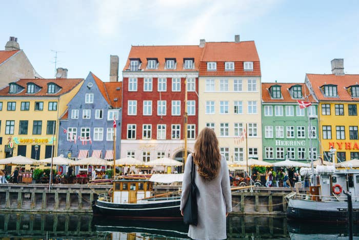 Woman standing facing historic colorful buildings and a docked boat