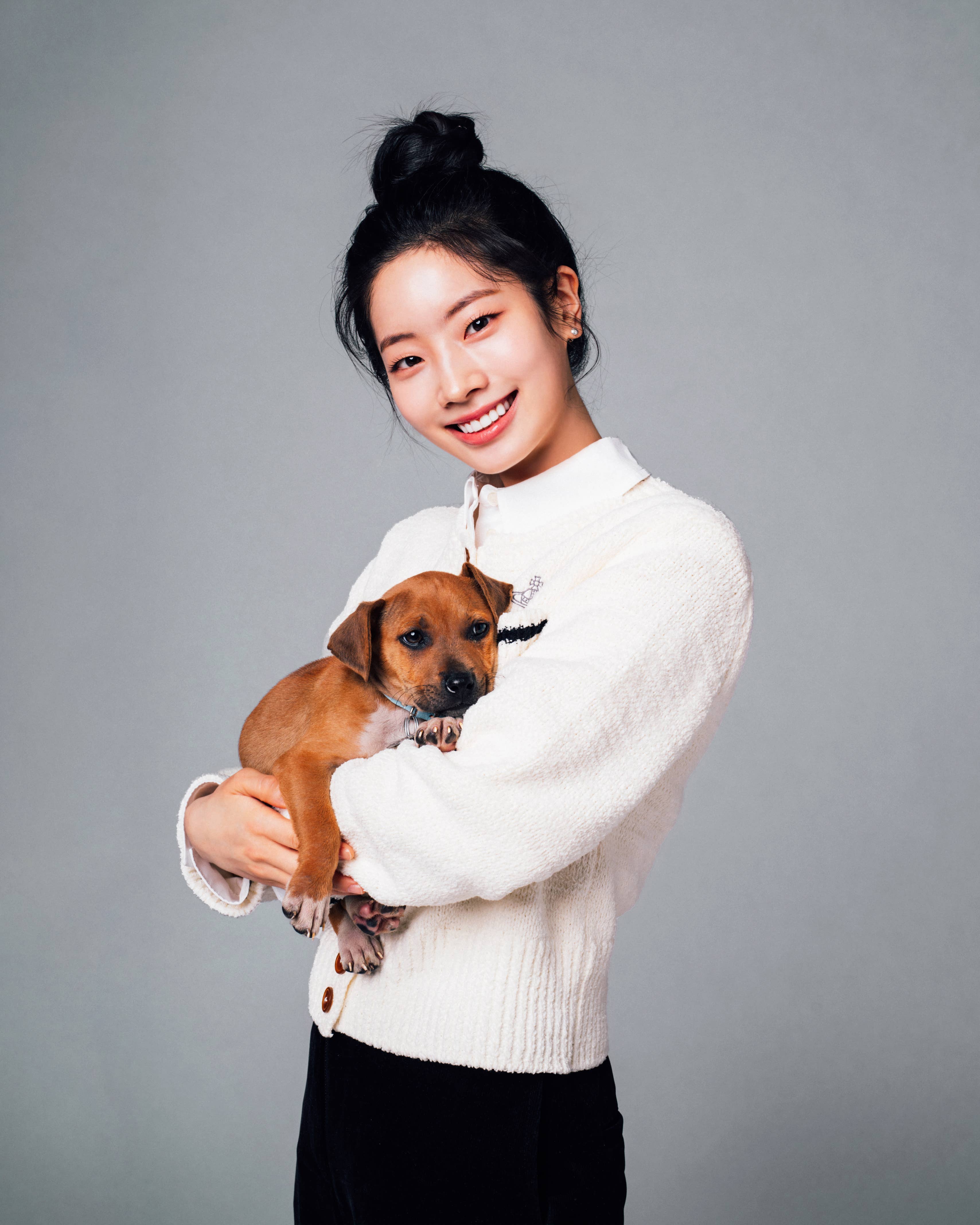 Woman smiling, holding a puppy, wearing a white top with a collar detail