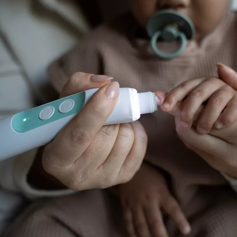 Adult&#x27;s hands holding a baby&#x27;s hands, using a baby nail trimmer on the baby&#x27;s fingernail