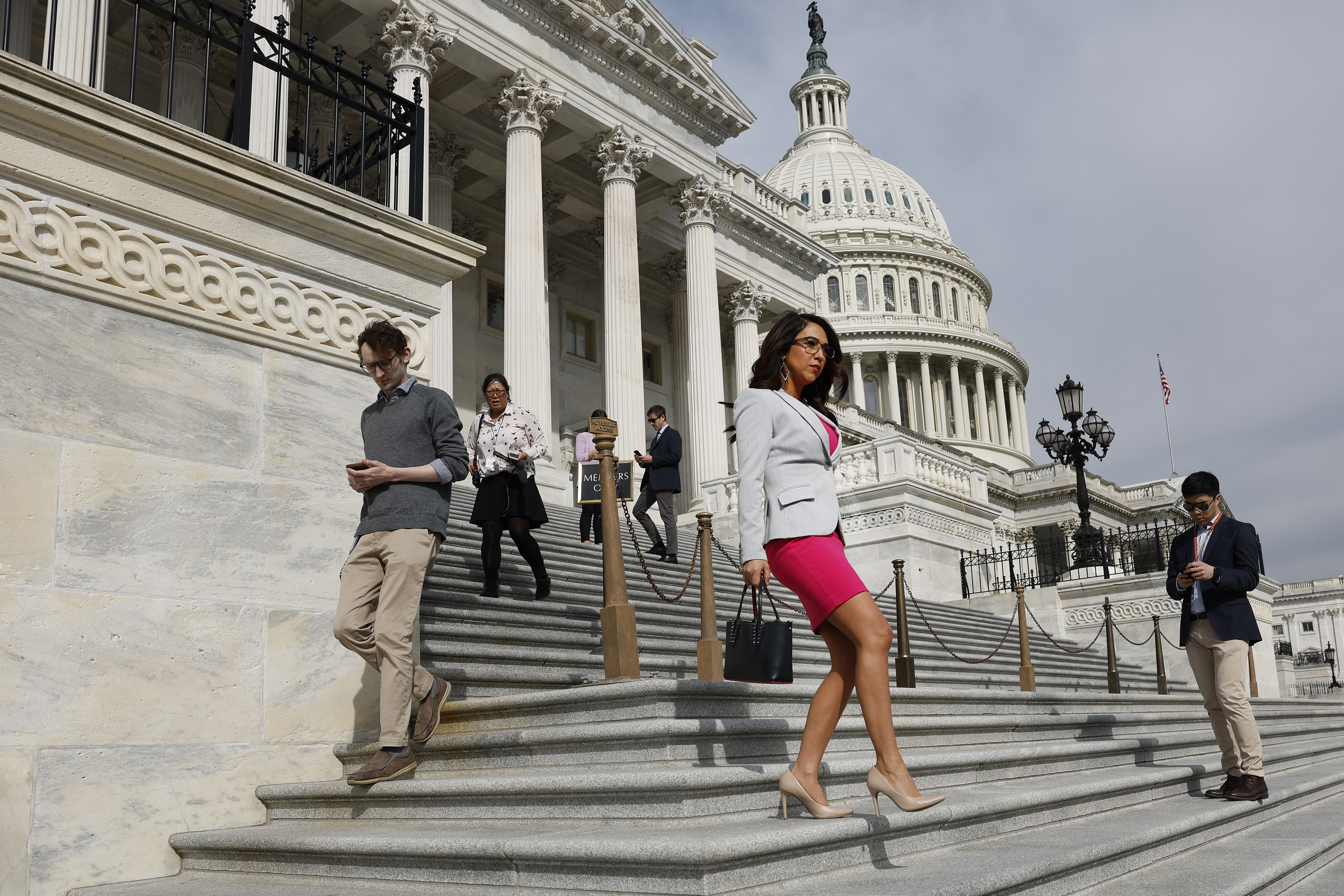 Individuals descend the Capitol steps, one in focus with a pink skirt and white blazer