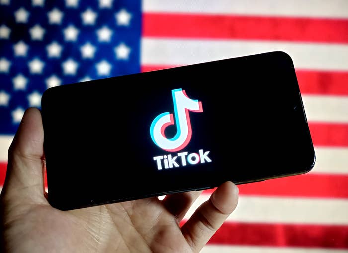 Hand holding a phone with the TikTok logo displayed, against a US flag background