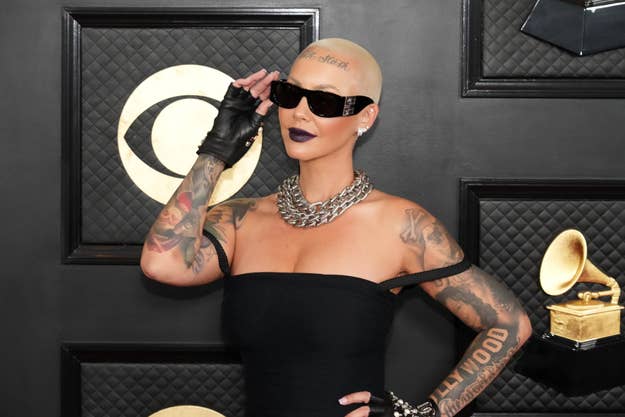 Person with tattoos in a black outfit and sunglasses posing at the Grammys