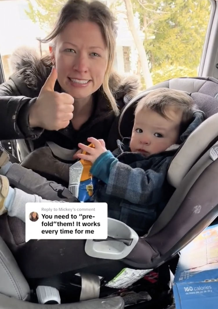 Woman giving a thumbs-up beside a child in a car seat; both smiling
